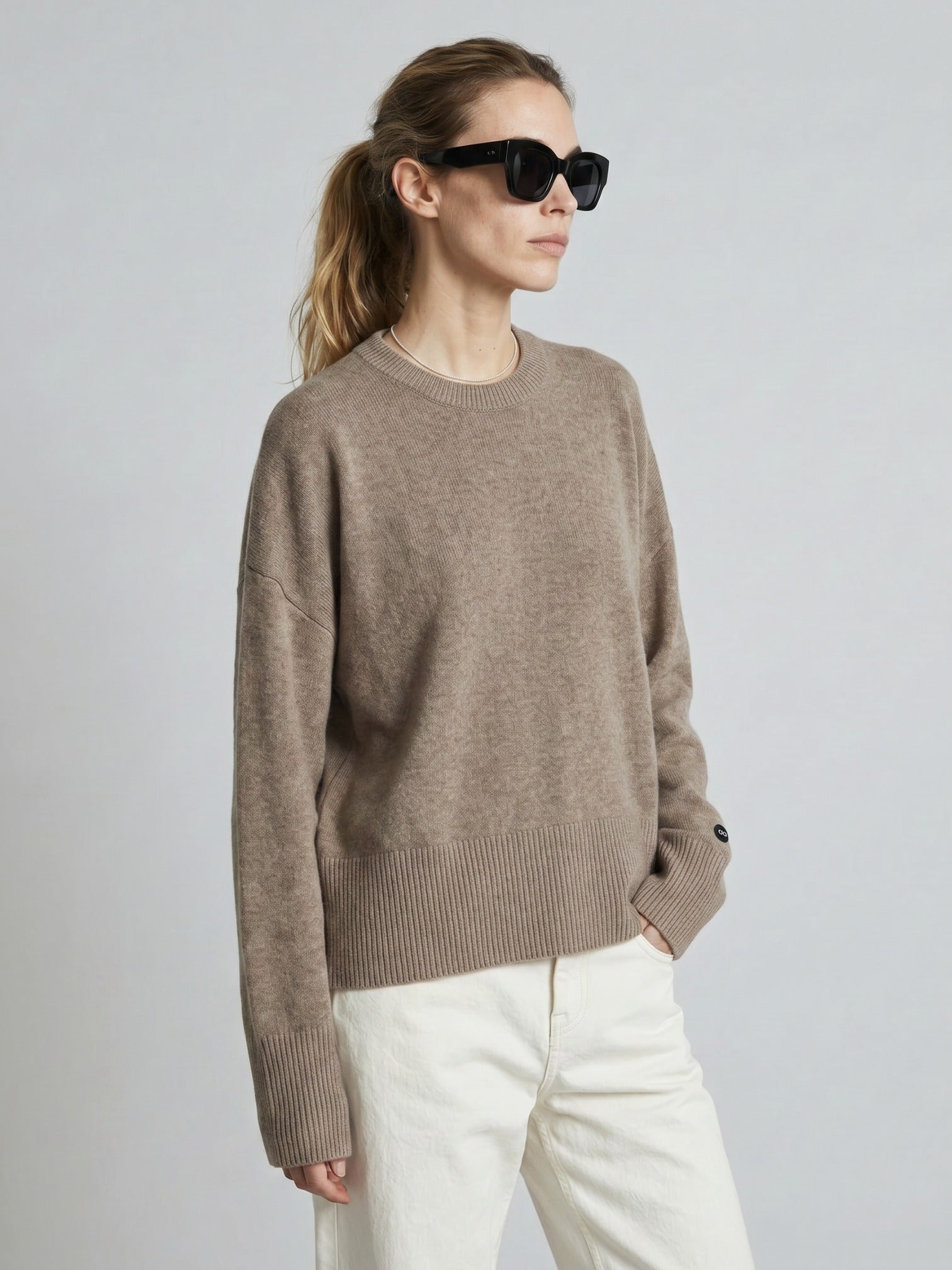 Woman wearing a brown sweater and sunglasses on a plain background