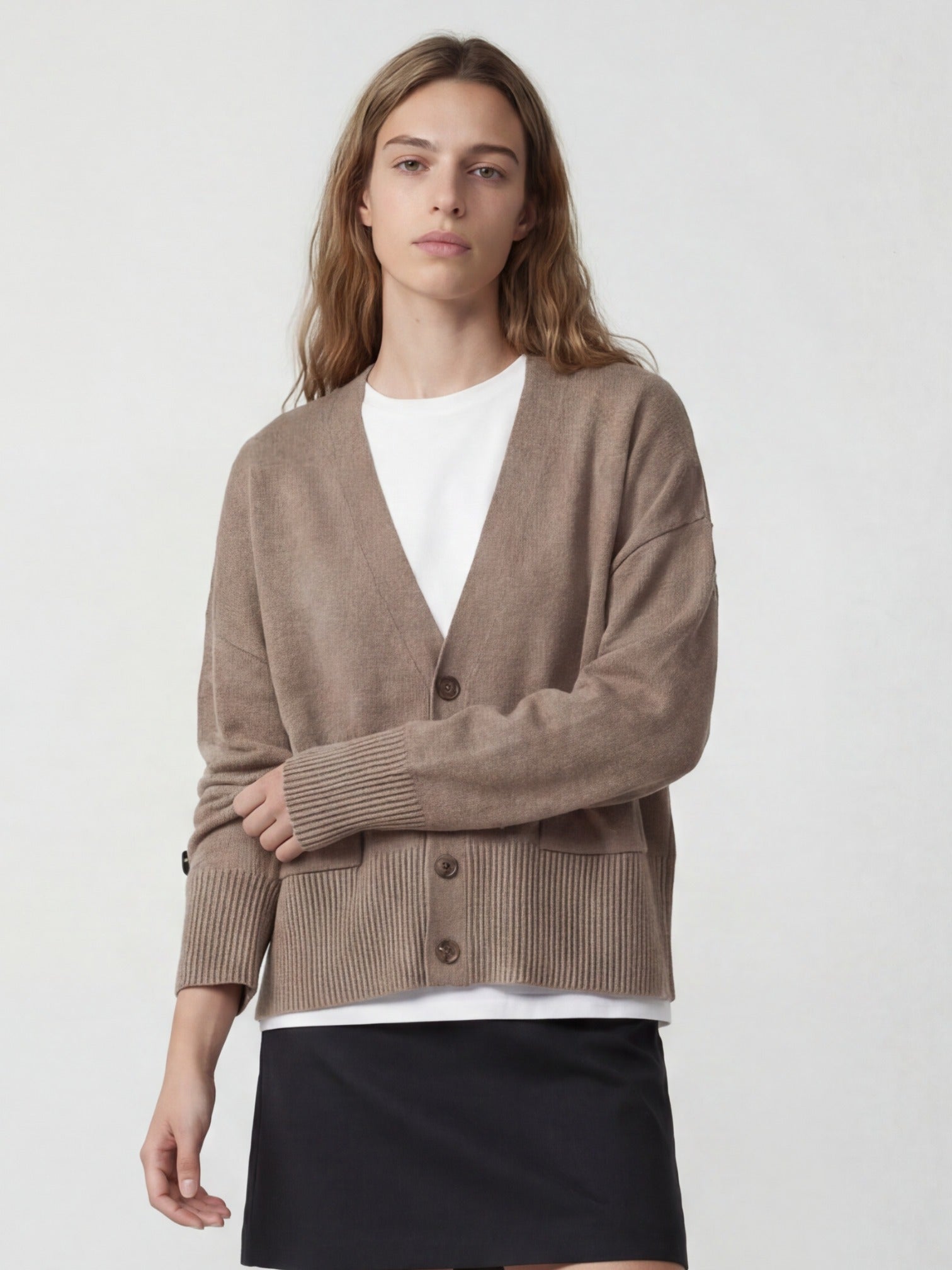 Woman wearing a brown cashmere cardigan over a white shirt and black skirt on a light gray background