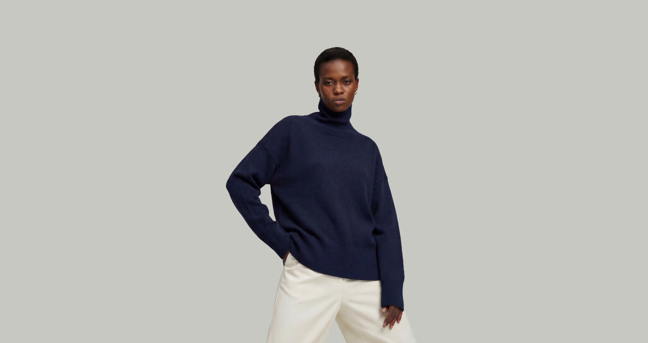 Woman wearing a navy cashmere sweater and white pants on a plain background