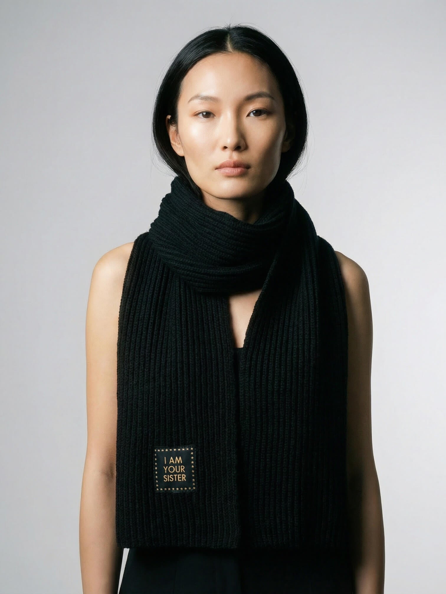 Woman wearing a black scarf with a visible brand logo on a gray background
