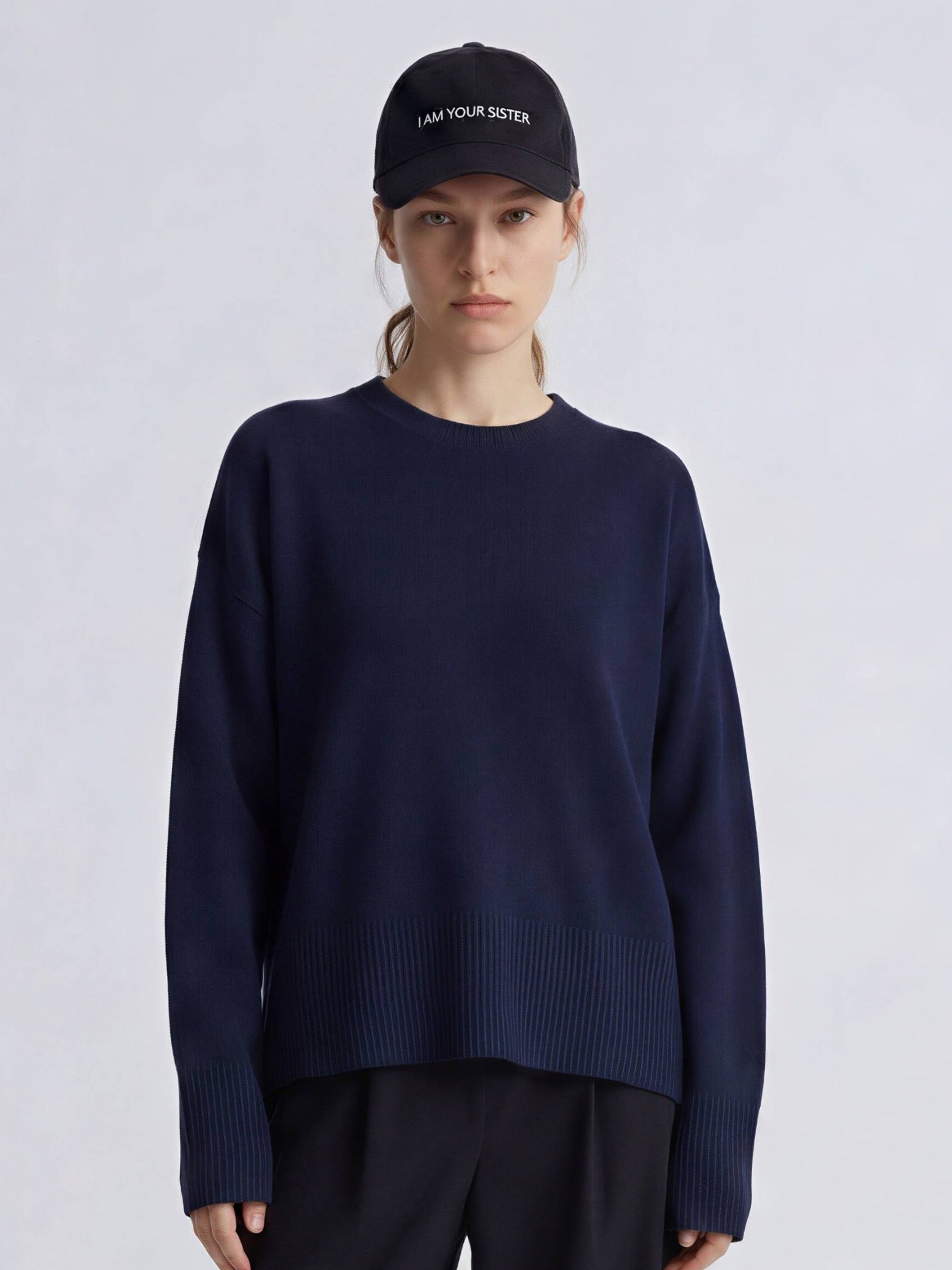 Woman wearing a navy sweater and black cap on a light gray background