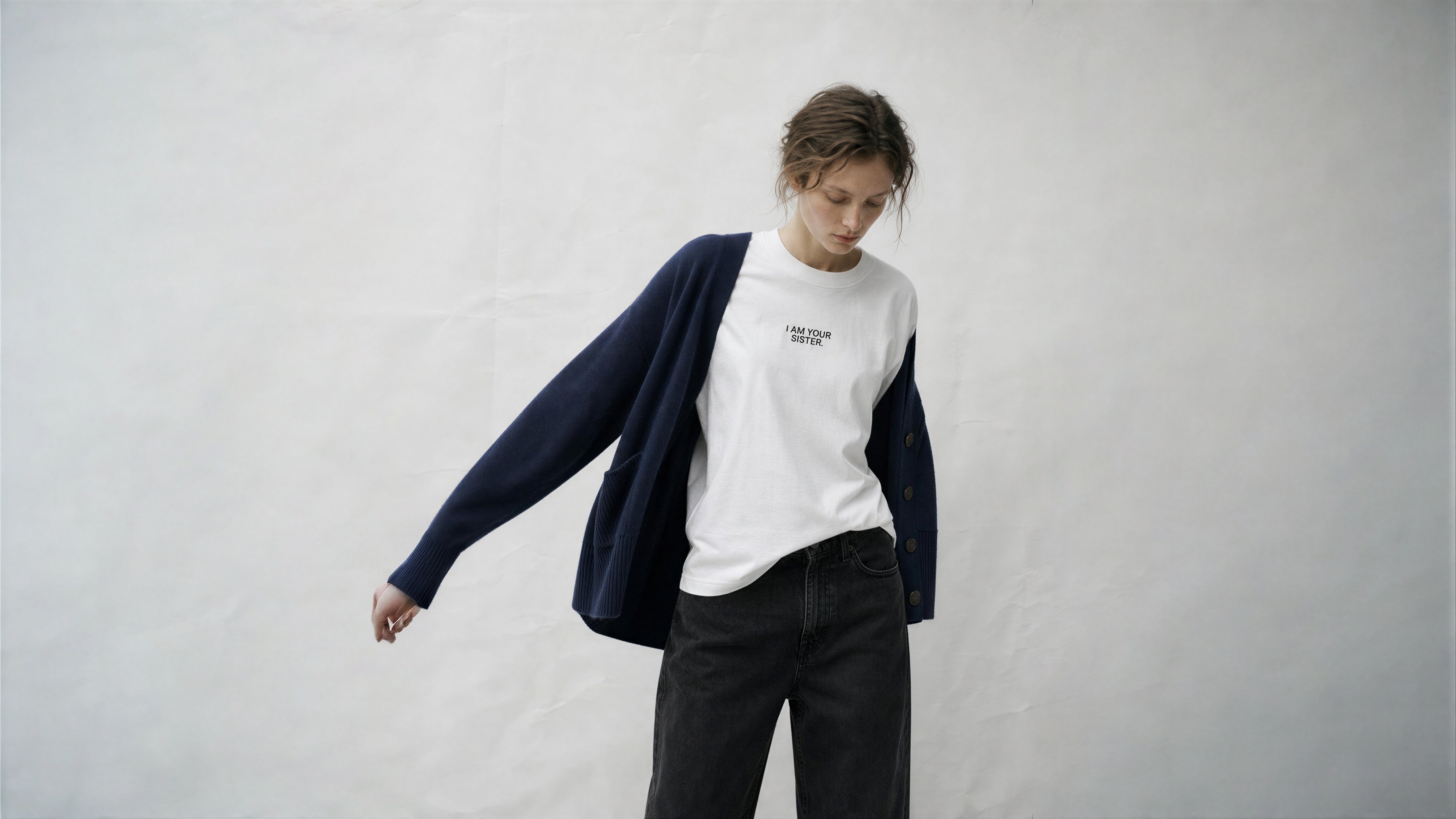 Person wearing a white sweatshirt with a logo and dark cardigan on a plain background