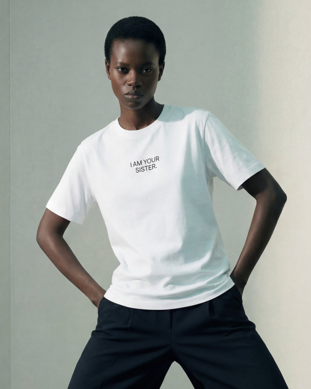 Woman wearing a white Sister Tee with 'I AM YOUR SISTER text on a plain background