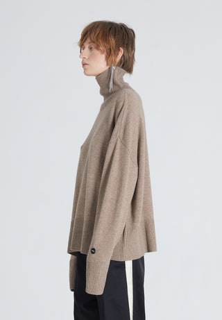 Woman wearing a high-end brown cashmere turtleneck. She also wears black pants and a silver earring 