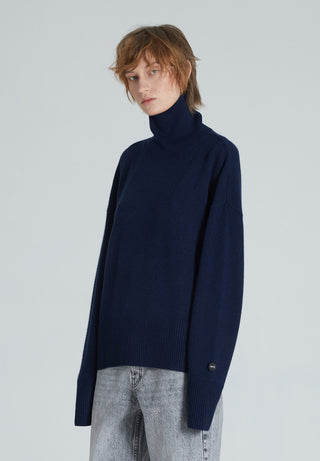 A navy turtleneck cashmere sweater with ribbed trims, displayed on a woman with a neutral expression.
