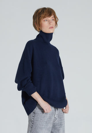 A woman wearing a navy cashmere turtleneck sweater with ribbed trims and a relaxed silhouette.